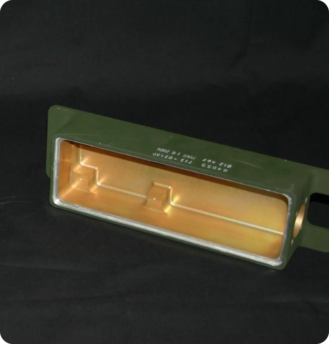 A rectangular metal case with a green exterior and a copper-toned interior, featuring a handle on one side and text imprinted on the top.