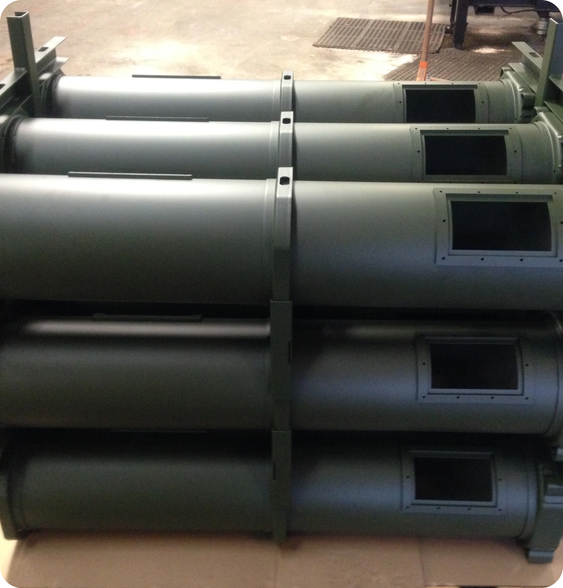 Six large cylindrical metal tubes stacked horizontally on a surface, each with rectangular openings on the side.