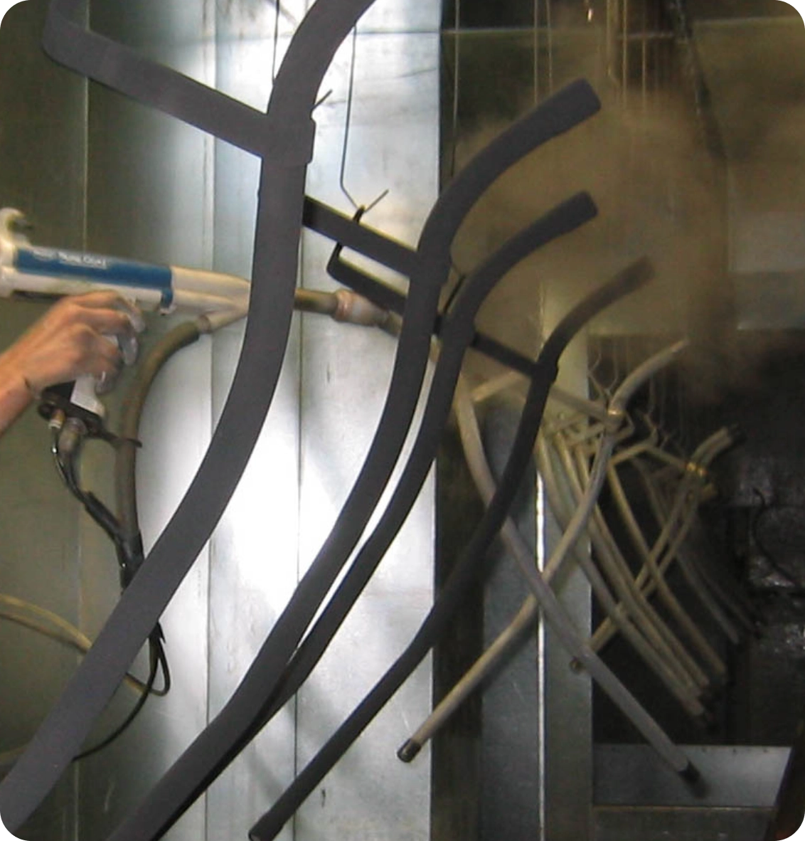 A person uses a spray gun to apply a coating to metal frames, which are lined up in a row in a workshop setting.